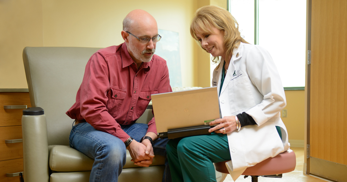 A female physician holding a laptop and clarifying questions and concerns about cancer with a patient